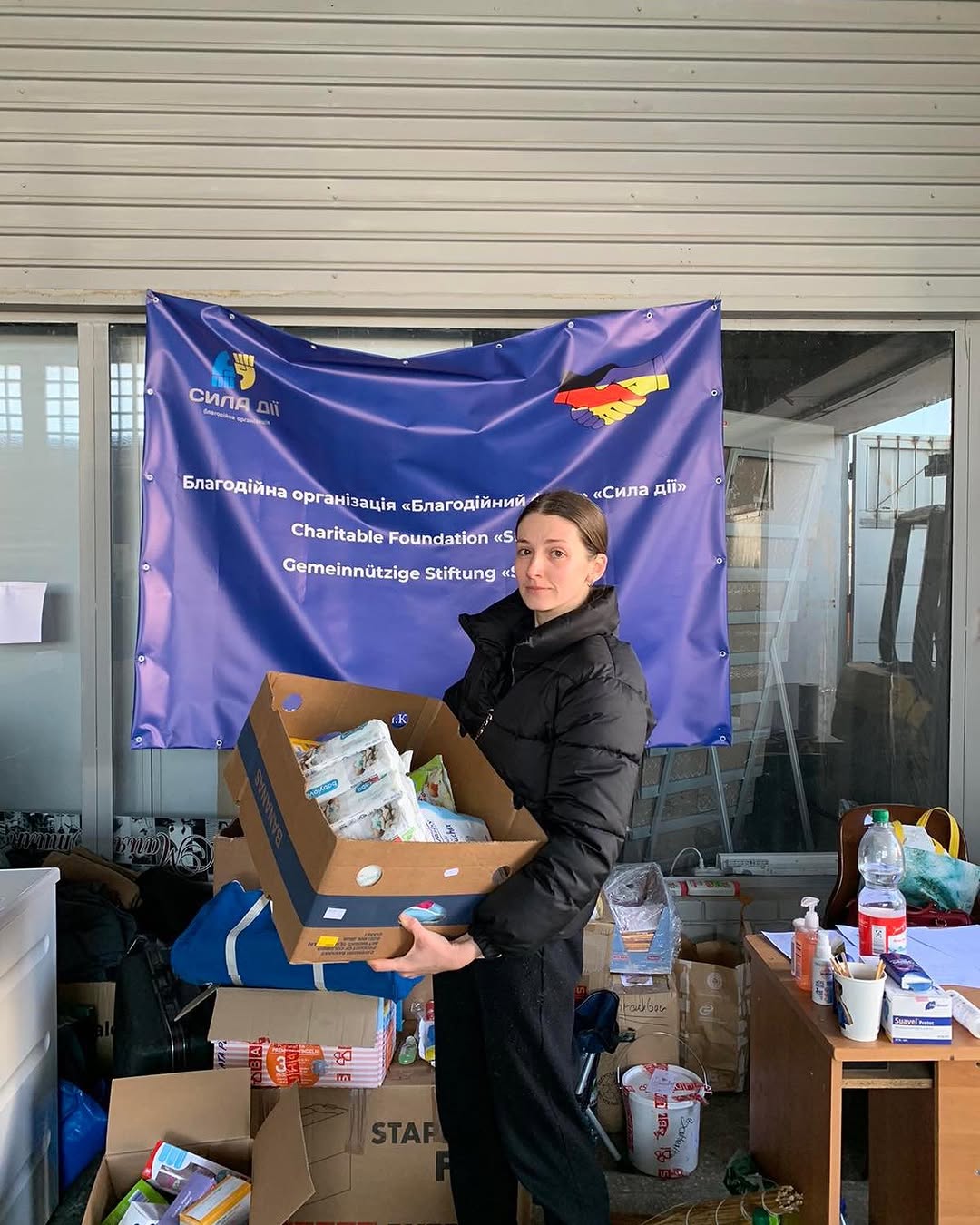 Helferin mit Hilfspaket vor dem Banner der Organisation Sila Dii